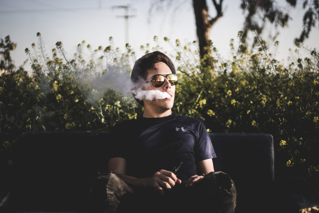 A person sitting on a bench outside using a dab pen